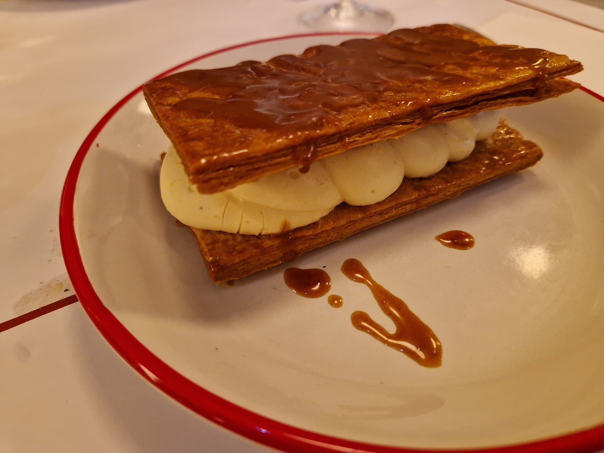 Milhojas de hojaldre caramelizado con crema, en un plato de borde rojo